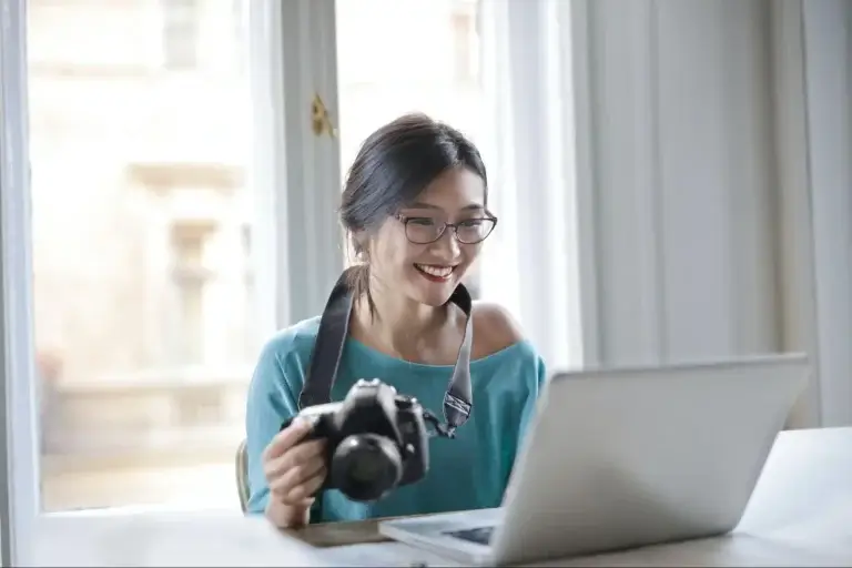 woman holding a camera sitting in front of laptop