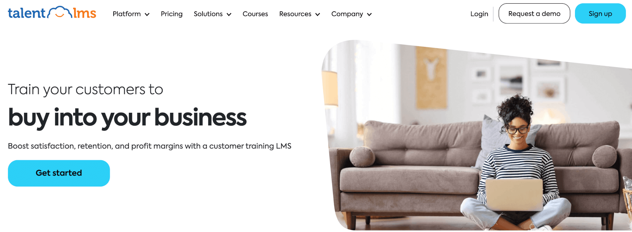 TalentLMS landing page sowing a woman sitting in front of a couch with a laptop on her lap