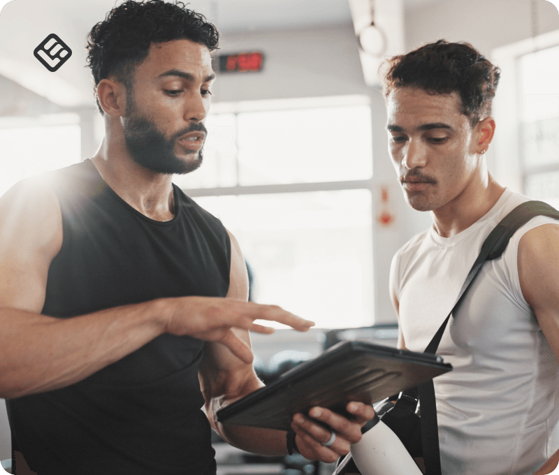 An image showing a coach holding a tablet and giving fitness advice to a trainee.