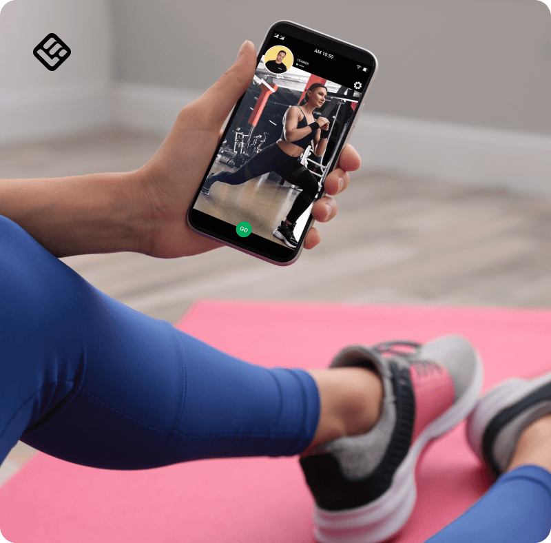 An image showing a woman exercising on a yoga mat while watching a fitness video on a mobile screen.